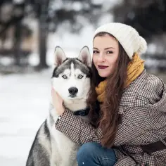 Dziewczyna w czapce i szaliku przytula husky. Czy husky szczekają? Ten piesek wygląda na bardzo spokojnego.