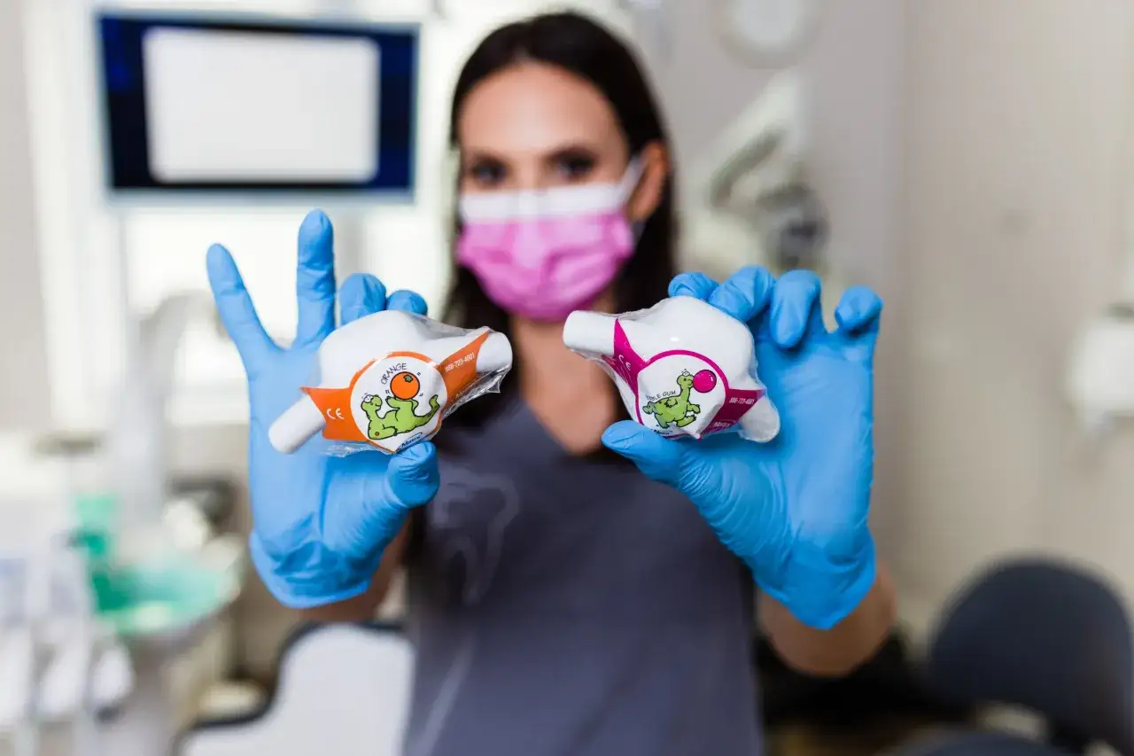 Dentystka w niebieskich rękawiczkach trzyma dwa opakowania